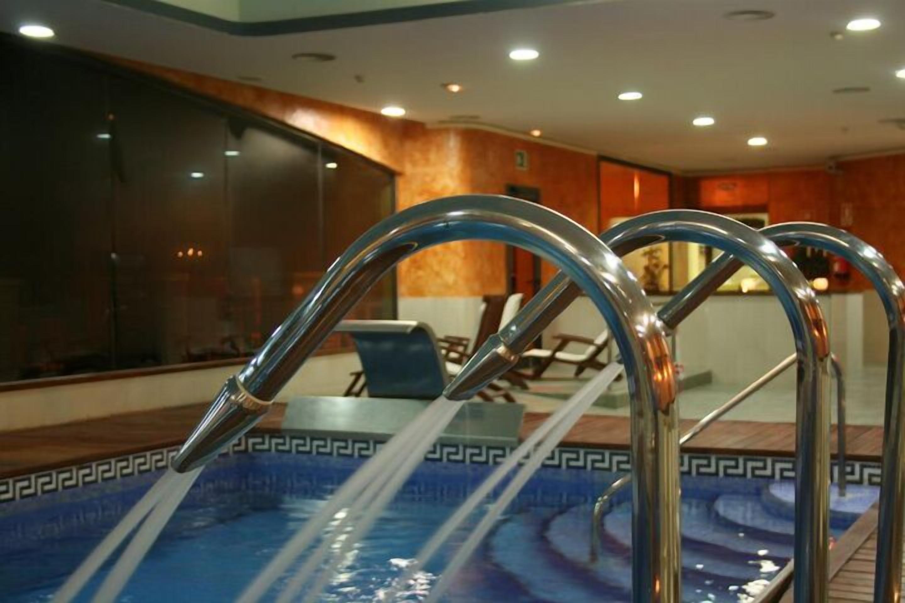 Una piscina con agua cristalina, escaleras metálicas y suelo de mosaico con un diseño geométrico.