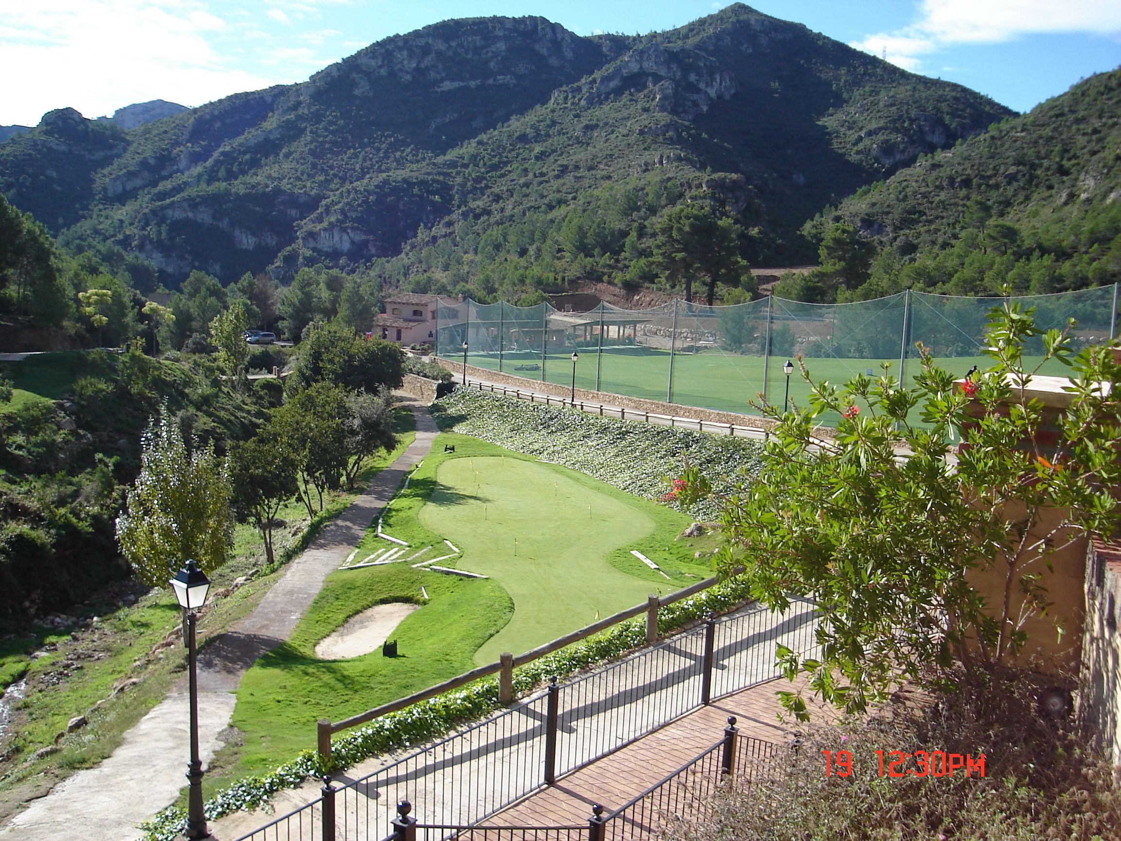 A golf course with a walking path, surrounded by greenery and mountains.