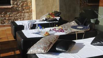 A sunlit outdoor seating area with stone walls, tables with white tablecloths, and black leather chairs.