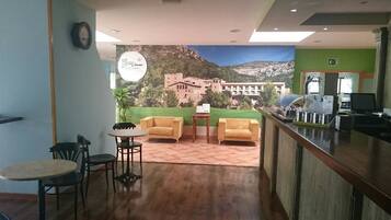 A reception area with a wooden floor, a reception desk, a seating area with two yellow armchairs and a small table, and a large poster of a mountainous landscape.