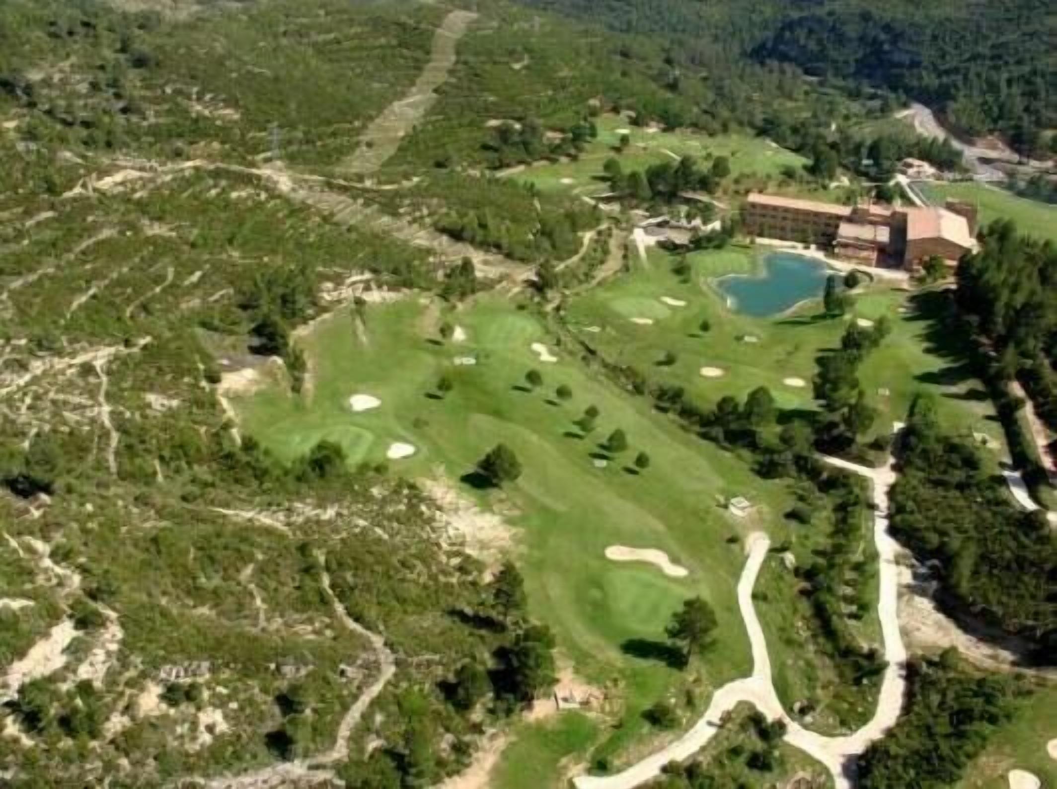 Vista aérea de un campo de golf con un club house, una piscina y zonas boscosas circundantes.