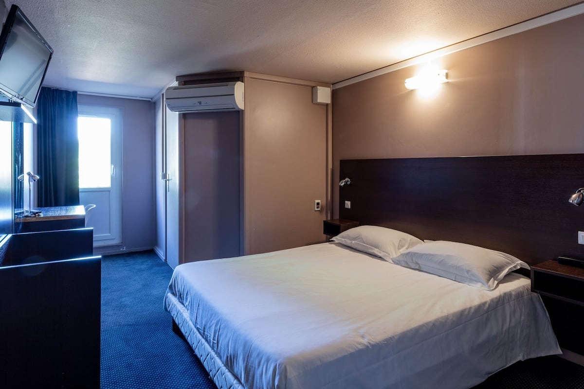Een hotelkamer met een bed, een televisie, een bureau en een raam met gordijnen.