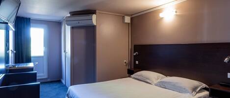 Habitación de hotel con cama, televisor, escritorio y ventana con cortinas.