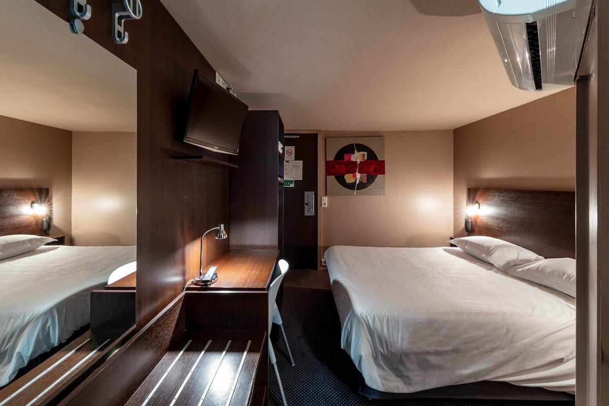 Een hotelkamer met twee bedden, een bureau, een stoel, een televisie en een airconditioner.