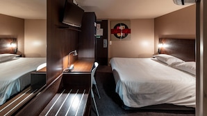 A hotel room with two beds, a desk, a chair, a TV, and a wall-mounted air conditioning unit.