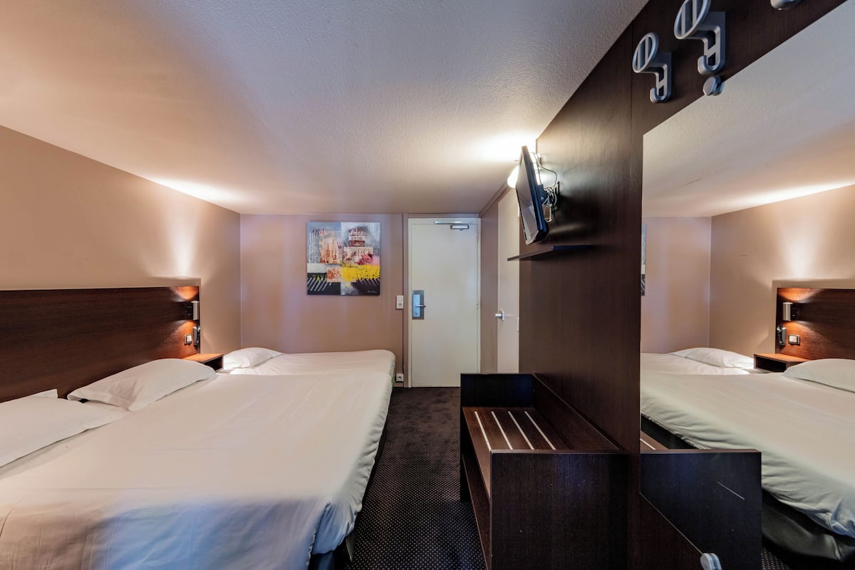 Habitación de hotel con dos camas, un escritorio pequeño, un espejo y un televisor montado en la pared.