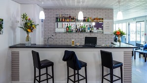 A bar area with a brick wall, bar stools, a laptop, and a variety of bottles.