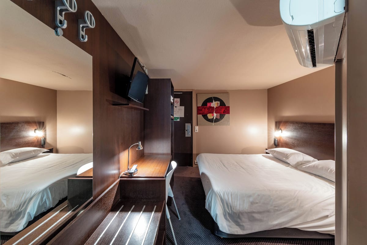 Een hotelkamer met twee bedden, een bureau, een televisie en een wandairconditioner.