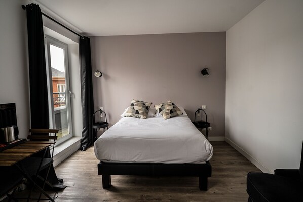 A bedroom with a bed, a window with curtains, a desk, and a chair.