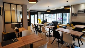 Un café moderno con mesas de madera y sillas negras y blancas, ventanas amplias y vistas a la calle.
