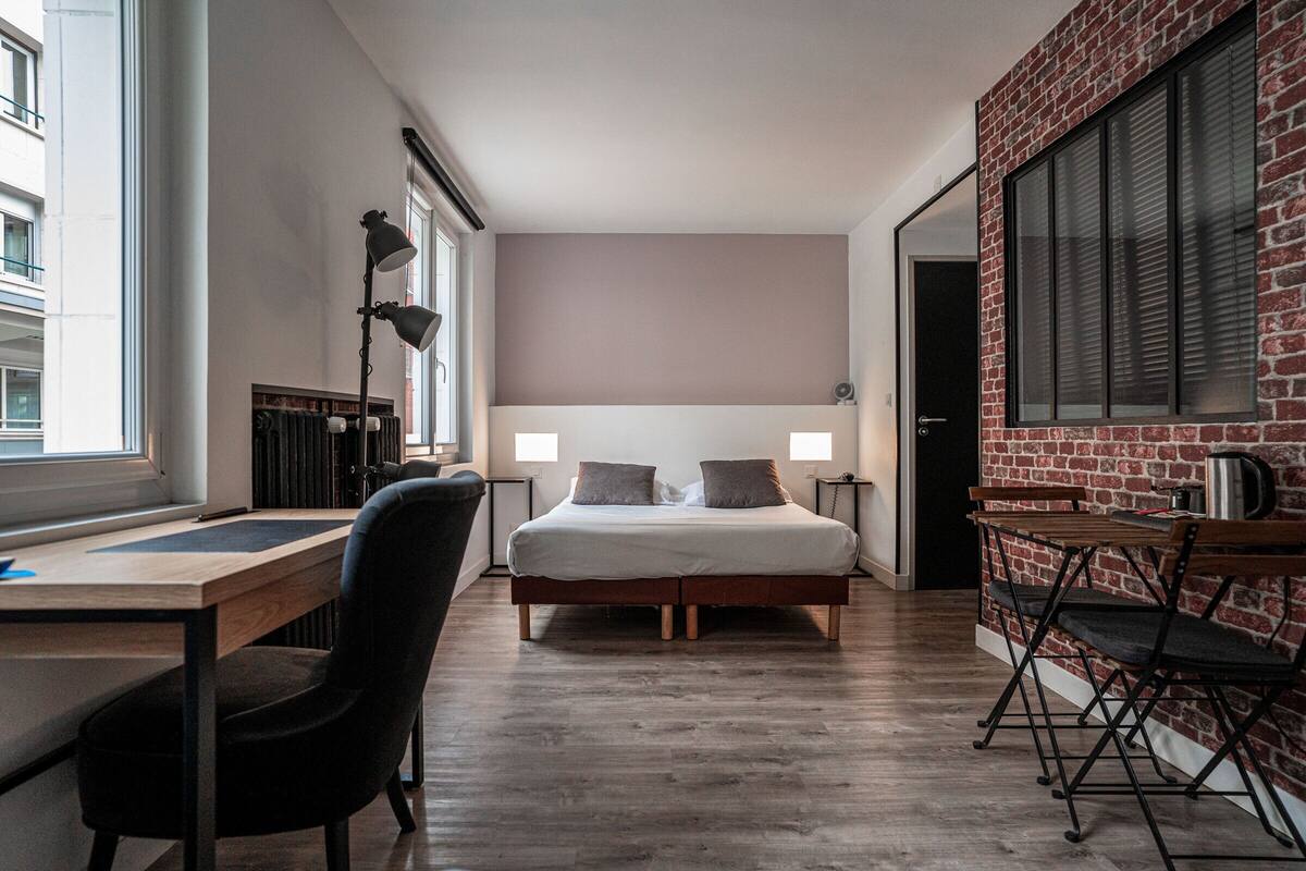 A modern hotel room with a large bed, a desk, and a dining area.