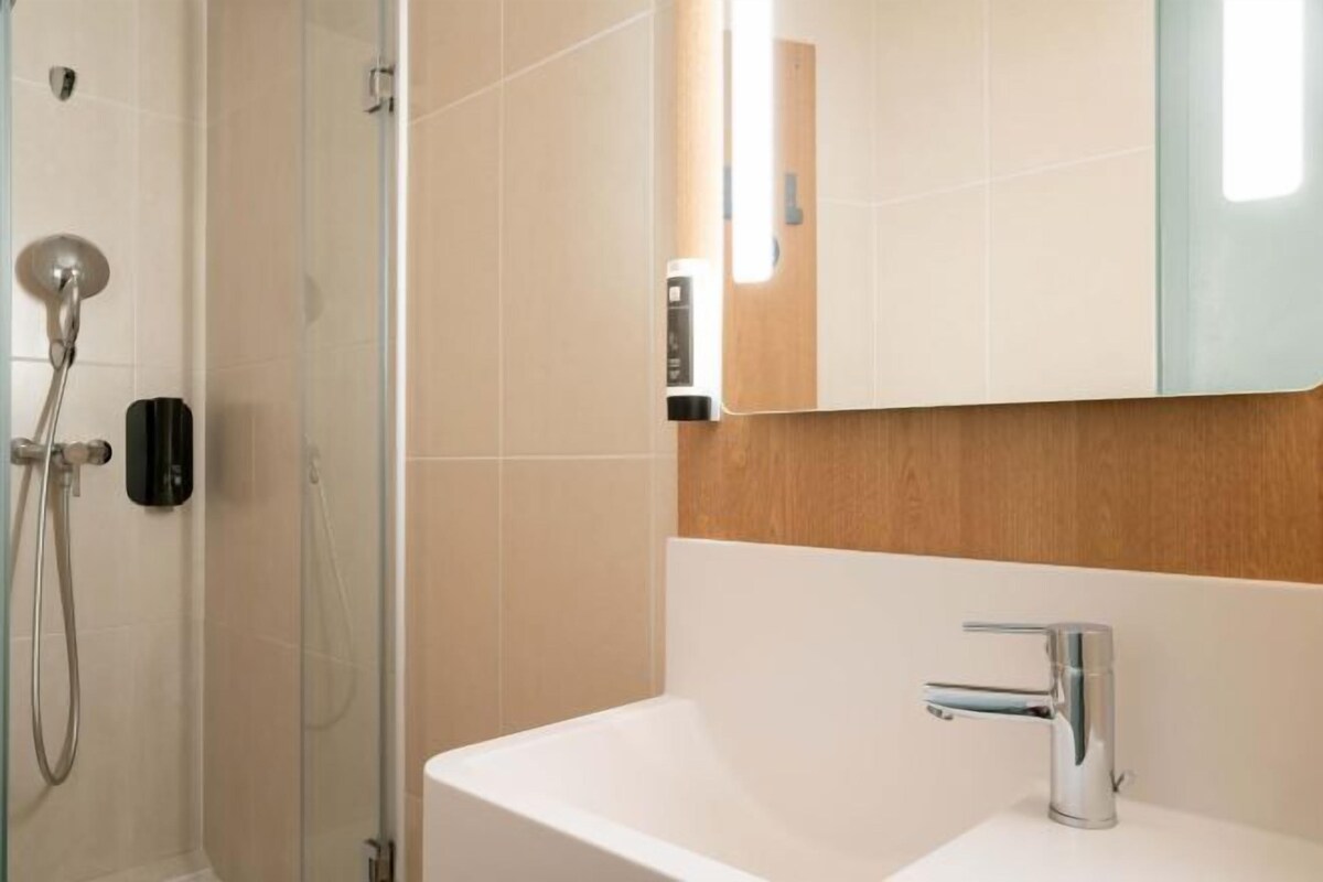 A modern bathroom with a glass shower enclosure, a white sink with a chrome faucet, and a wooden panel above the sink.