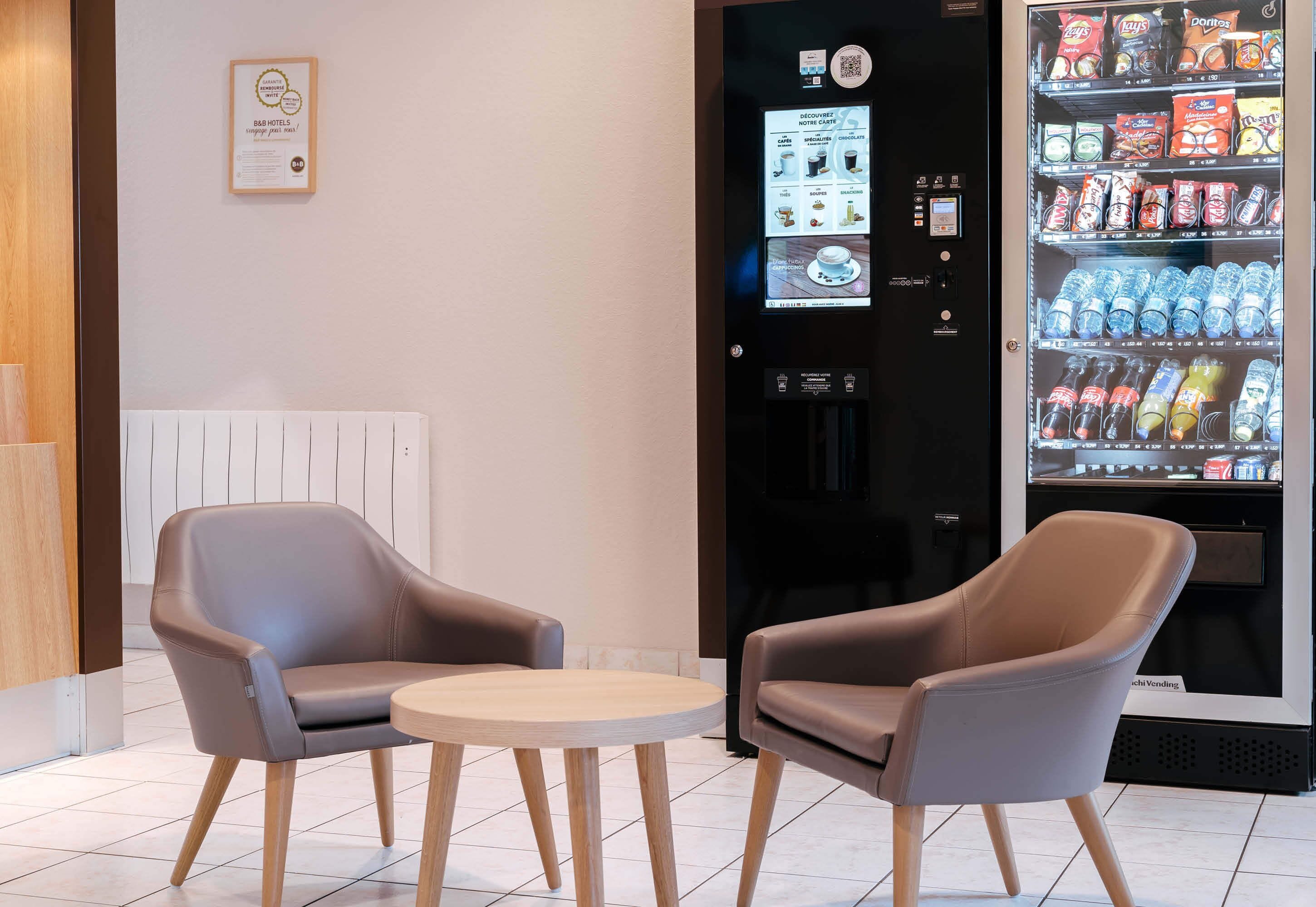 A modern hotel lobby with two leather armchairs, a vending machine, and a refrigerator stocked with beverages.