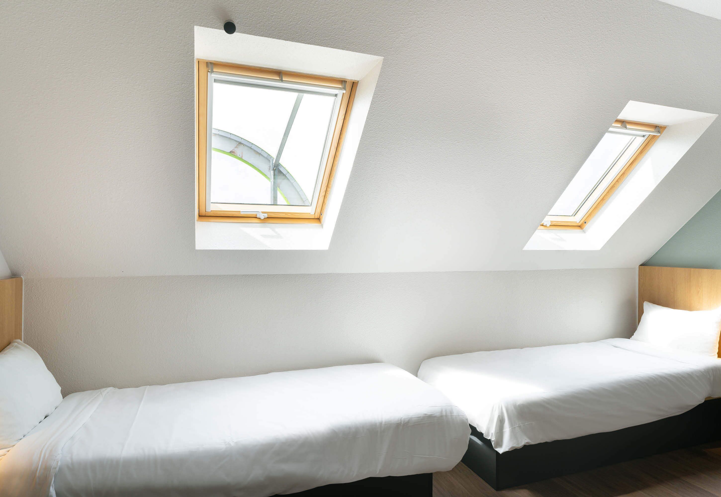 Una habitación con dos camas, techo inclinado y tragaluces.