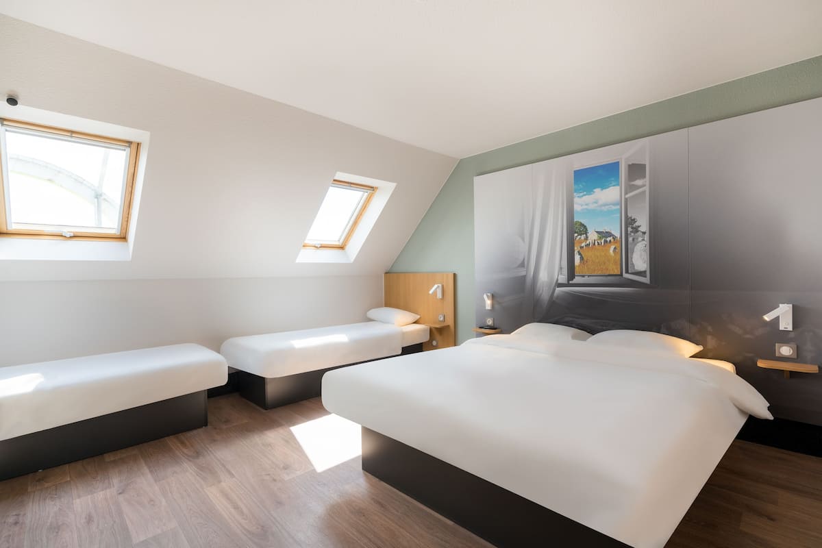 Una habitación de hotel moderna con dos camas, un tragaluz, un cuadro y suelo de madera.