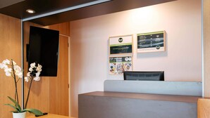 Et reception område med et træskrivebord, en potteplante og et fladskærms-tv monteret på væggen.