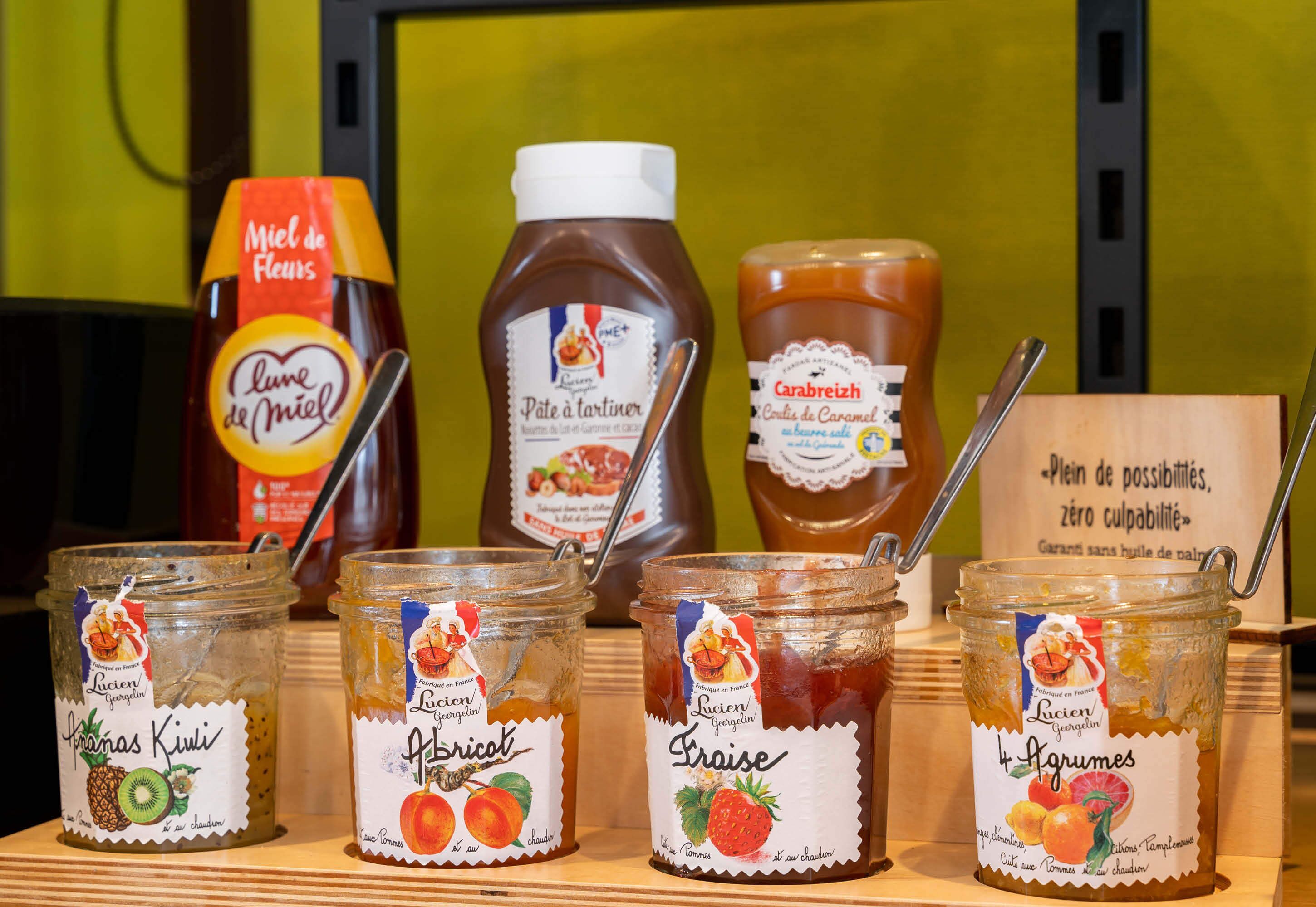 Various jars of preserves and sauces on a wooden shelf.