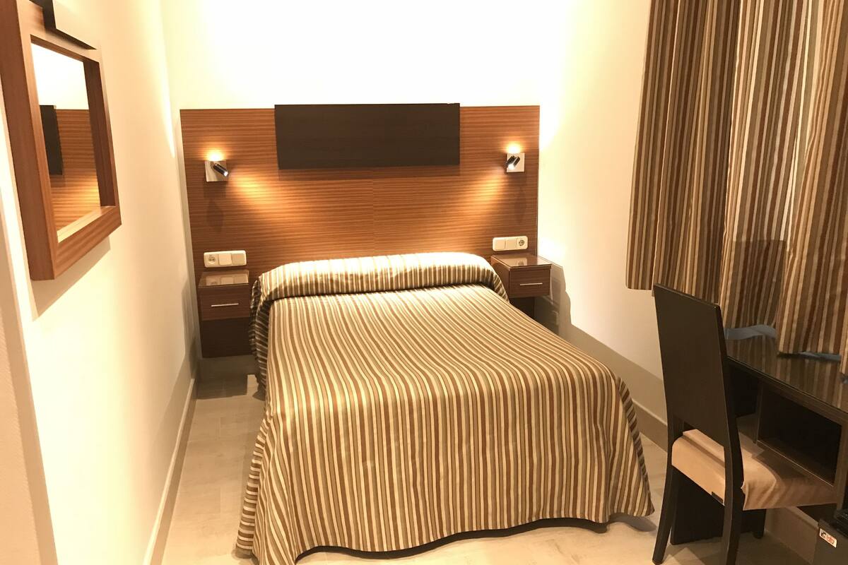 A modern hotel room with a large bed, bedside tables, a desk, and a chair.