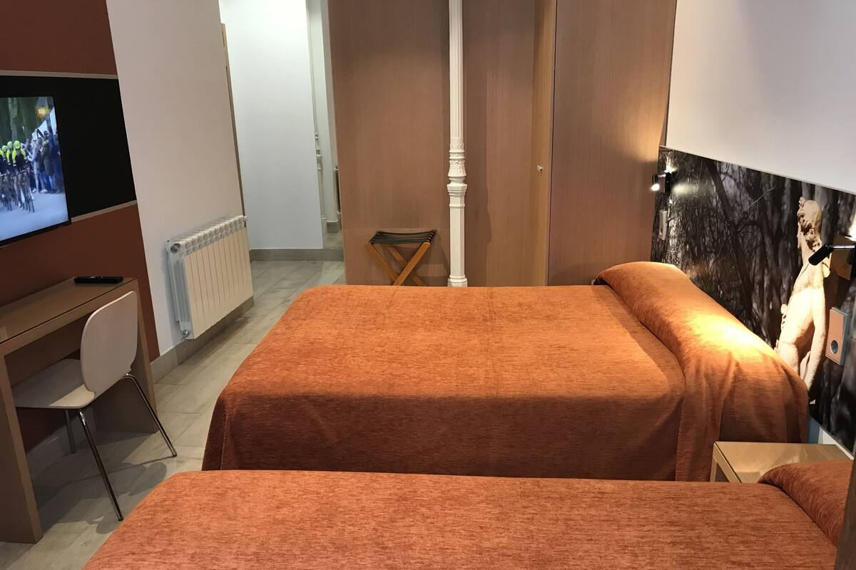 A hotel room with two beds, a desk, a chair, a television, and a poster on the wall.