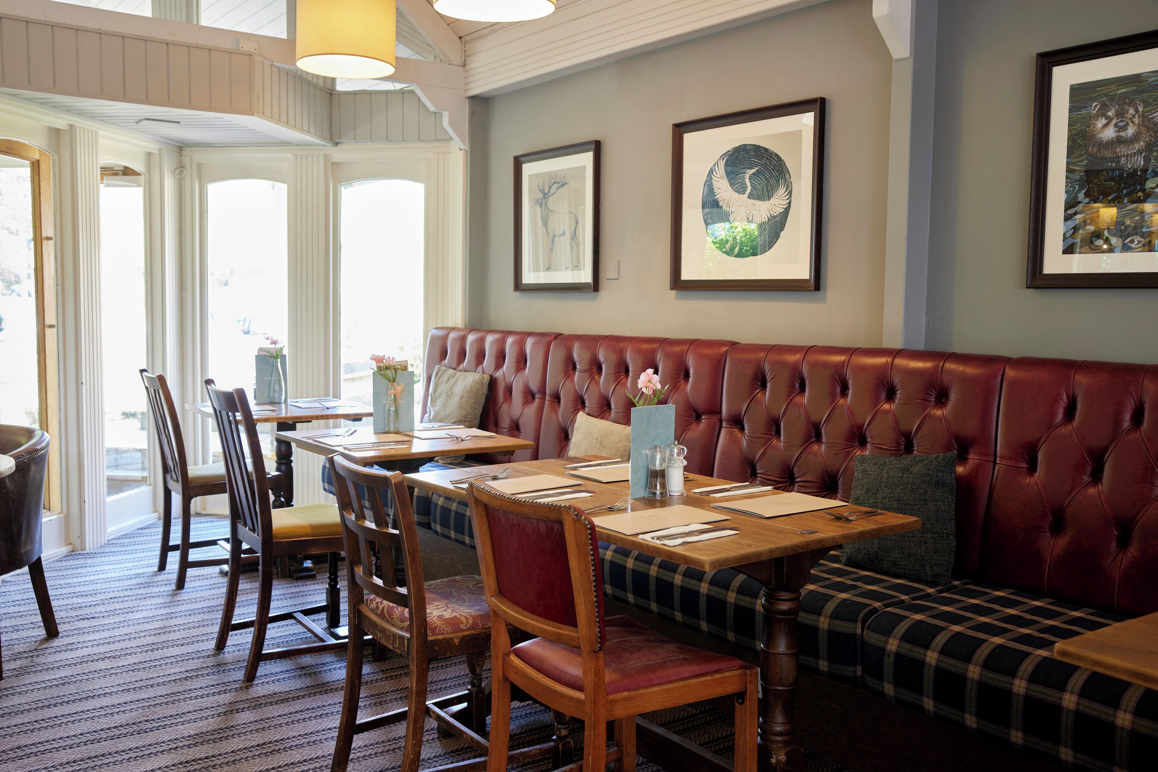 A restaurant with a red upholstered bench, wooden tables, and chairs. There are framed pictures on the wall.