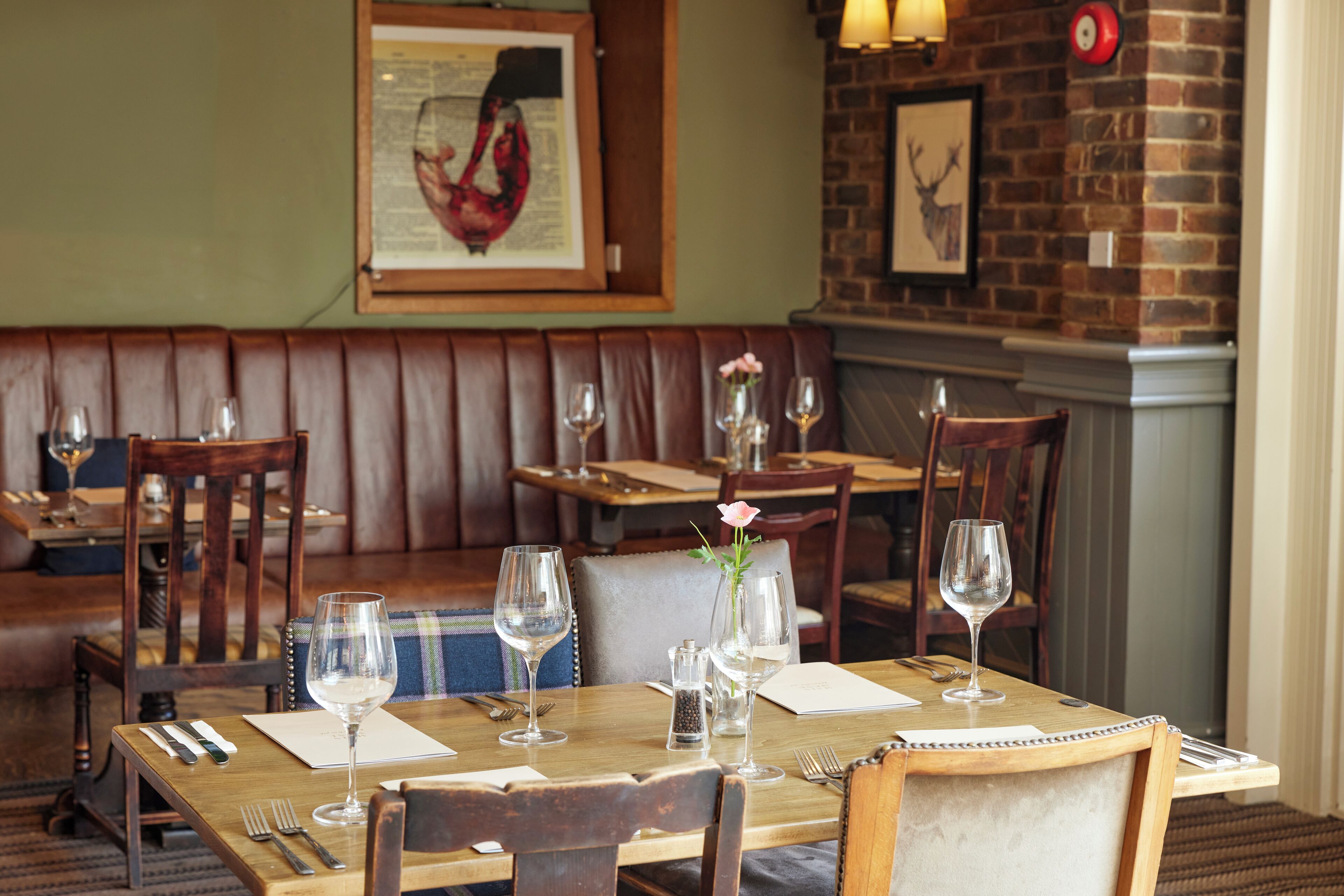 A restaurant with wooden tables and booths, each set with wine glasses, cutlery, and menus.