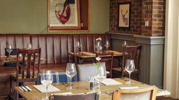 A restaurant with wooden tables and booths, each set with wine glasses, cutlery, and menus.