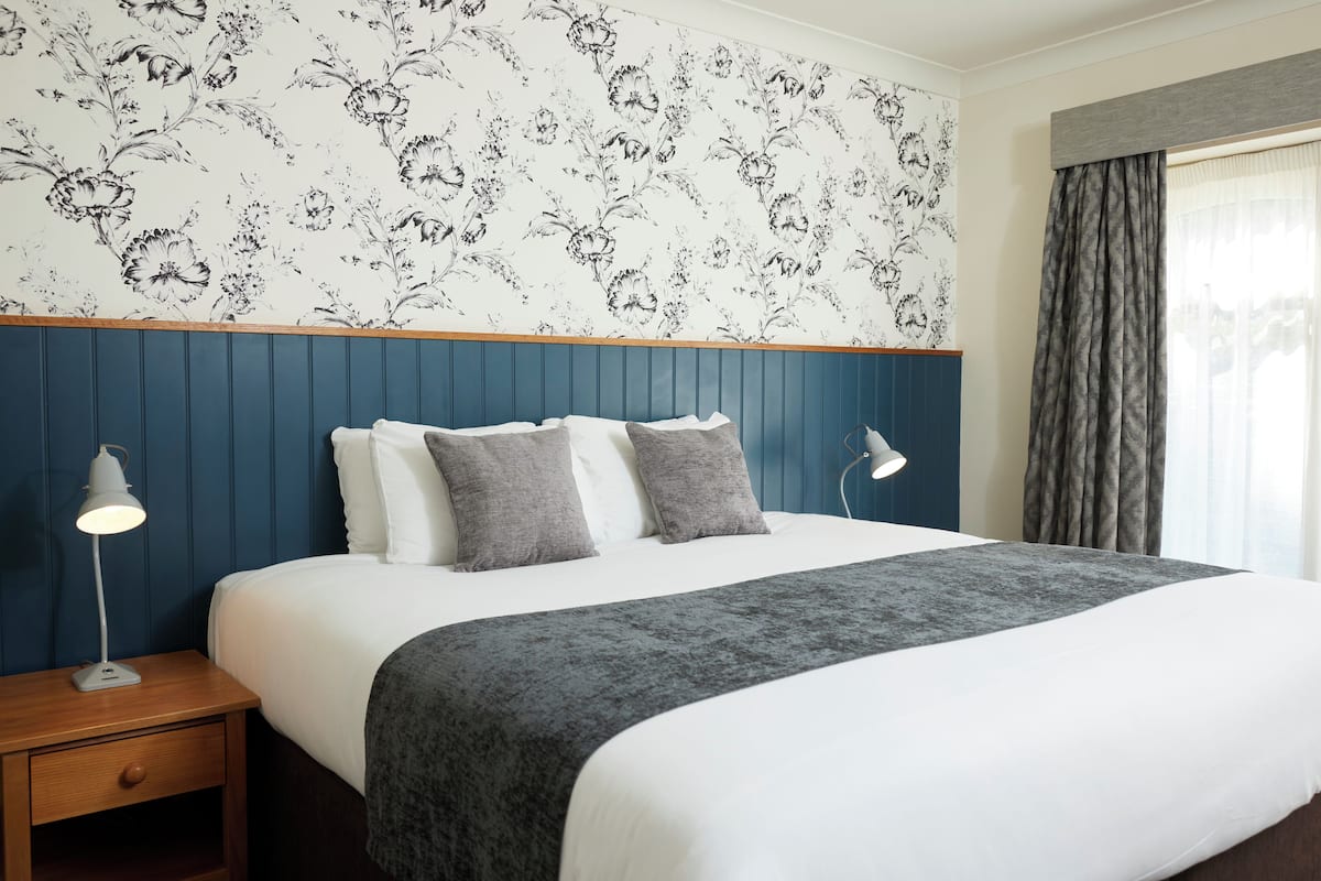 A neatly made bed with a grey blanket, two grey pillows, and a white duvet.