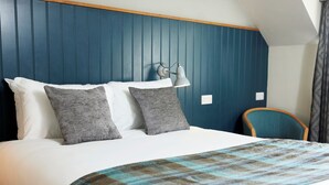 A neatly made bed with white linens and two gray pillows, a plaid blanket, a wall-mounted lamp, and a teal chair. - St Leonard's Hotel by Greene King Inns (Ringwood)
