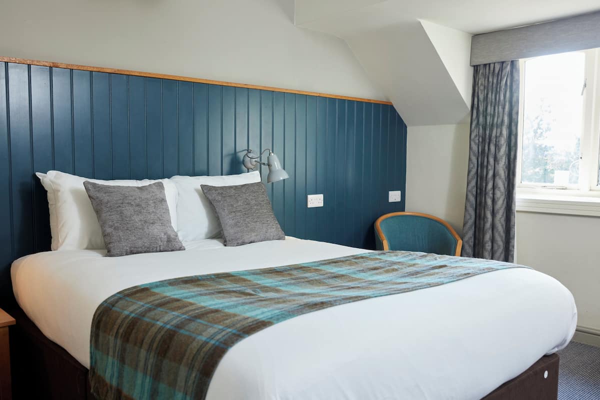 A hotel room with a bed, a nightstand, a chair, a lamp, and a window with curtains.