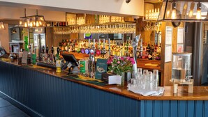 A bar area with a counter, bar stools, a cash register, and a variety of bottles and glasses. - St Leonard's Hotel by Greene King Inns (Ringwood)