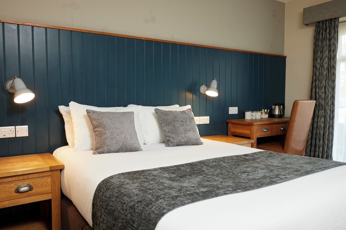 A hotel room with a large bed, two bedside lamps, a wooden nightstand, a wooden dresser, and a chair.