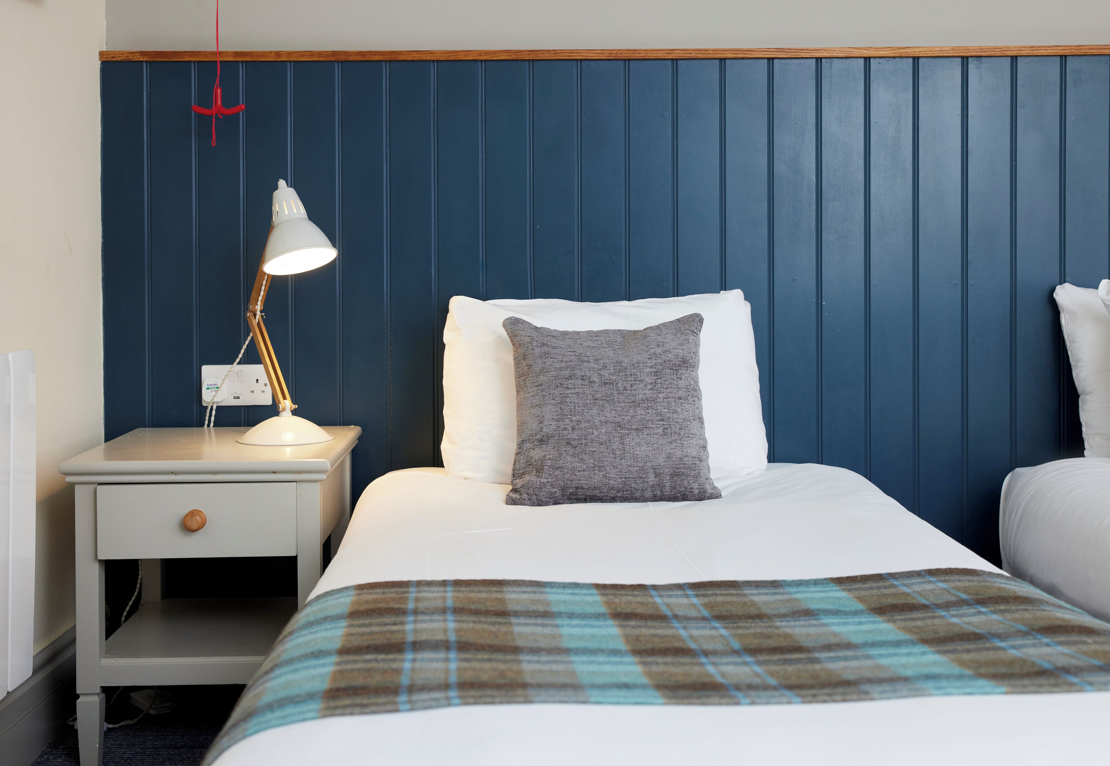 A neatly made bed with a plaid blanket, a bedside lamp, and a nightstand with a drawer.