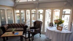 A room with a leather sofa, a wooden coffee table, a dining table with a white tablecloth, and a vase of flowers. - St Leonard's Hotel by Greene King Inns (Ringwood)