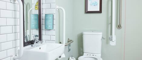 A bathroom with a white sink, a toilet, and a handrail.