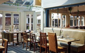 An indoor dining area with wooden tables and chairs, a bench, and hanging light fixtures. - St Leonard's Hotel by Greene King Inns (Ringwood)