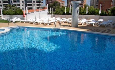 Una piscina al aire libre, sombrillas, sillones reclinables de piscina