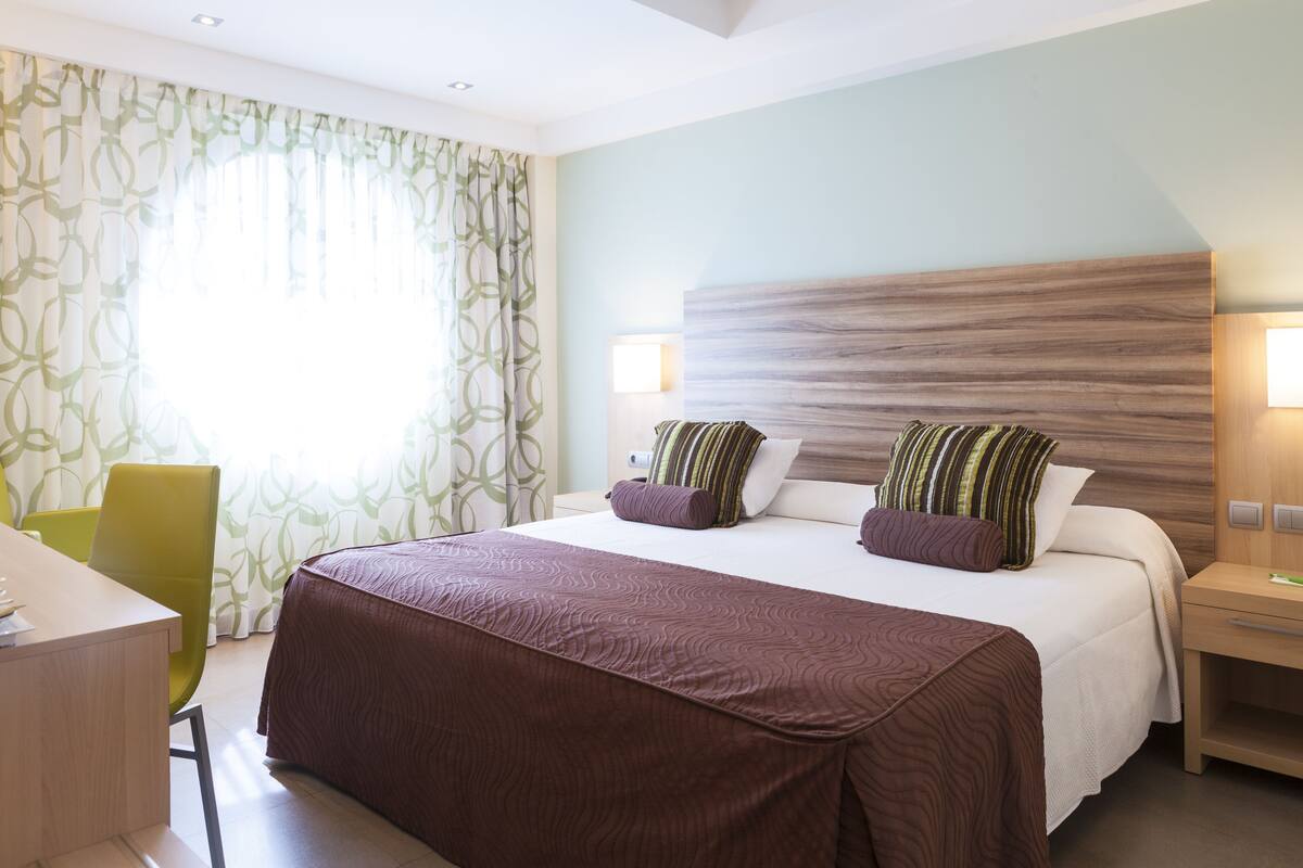A hotel room with a bed, a desk, a chair, and a nightstand.