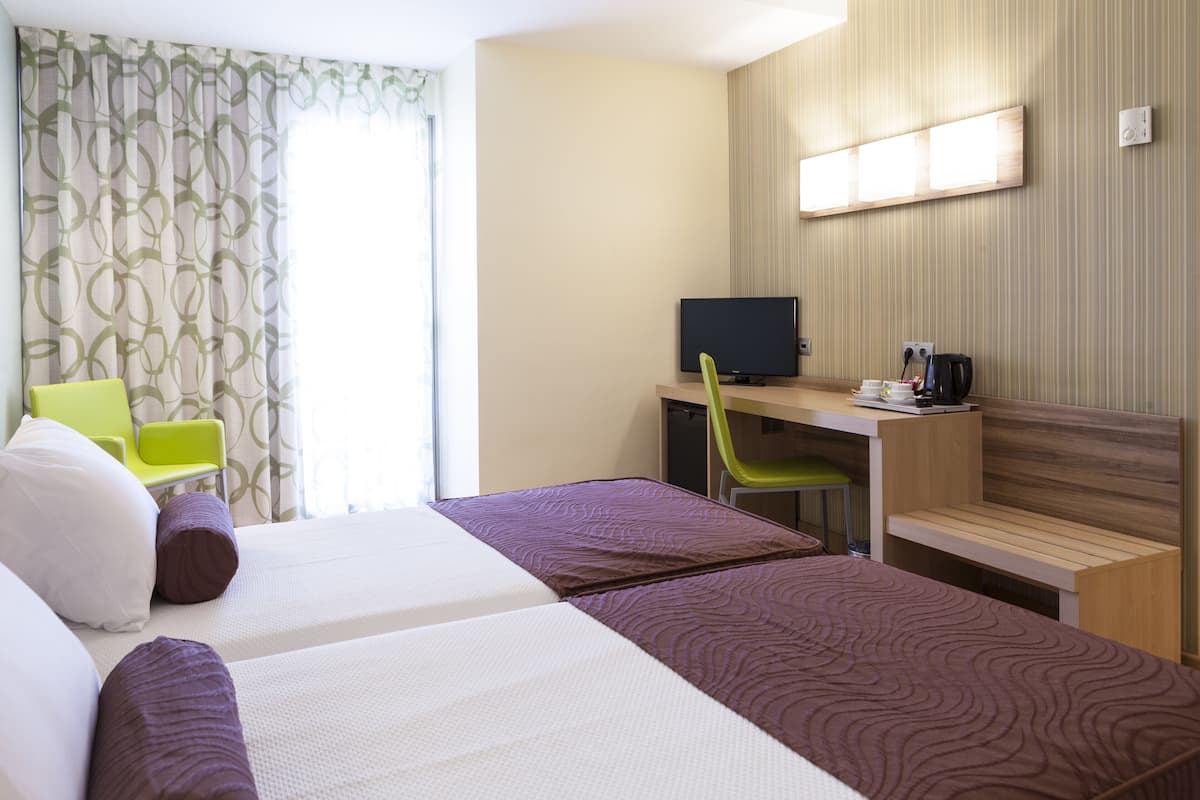 A hotel room with two beds, a desk with a computer, a chair, and a television.