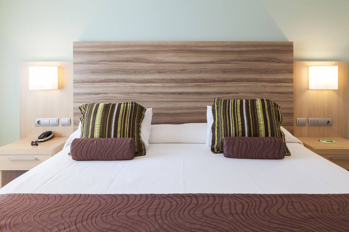 A double bed with a wooden headboard, two bedside lamps, and a telephone on the left nightstand.