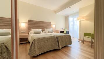 A hotel room with two beds, a desk, a chair, and a lamp.