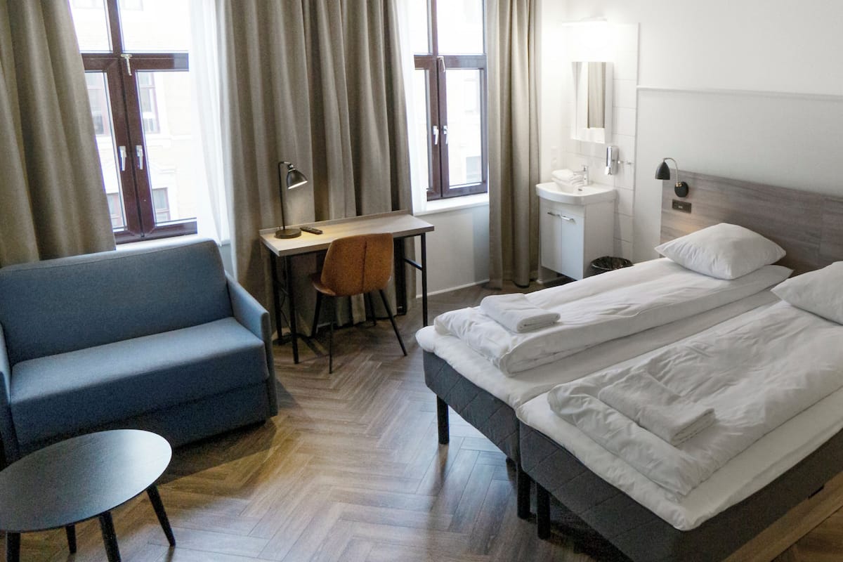 Une chambre d’hôtel avec un lit, un bureau, une chaise, une petite table et une fenêtre avec des rideaux.