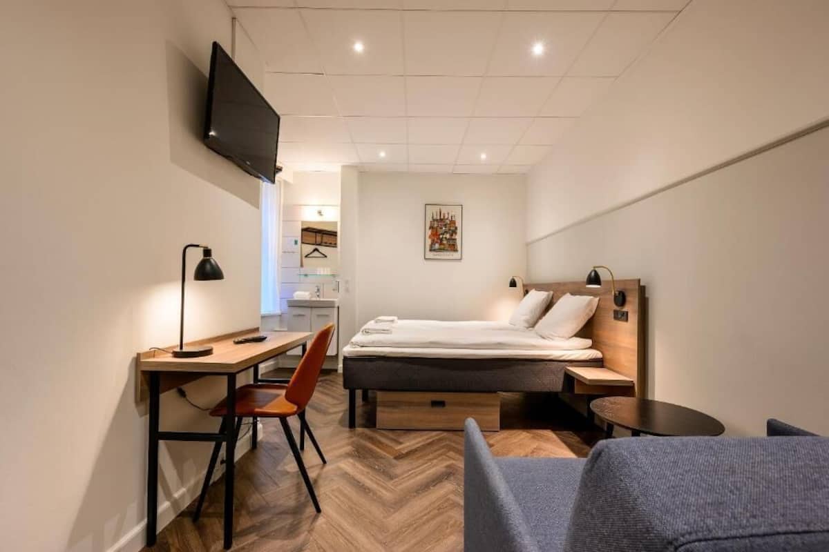 Une chambre d’hôtel de taille réduite, comprenant un lit, un bureau, une chaise, une télévision et une petite table.