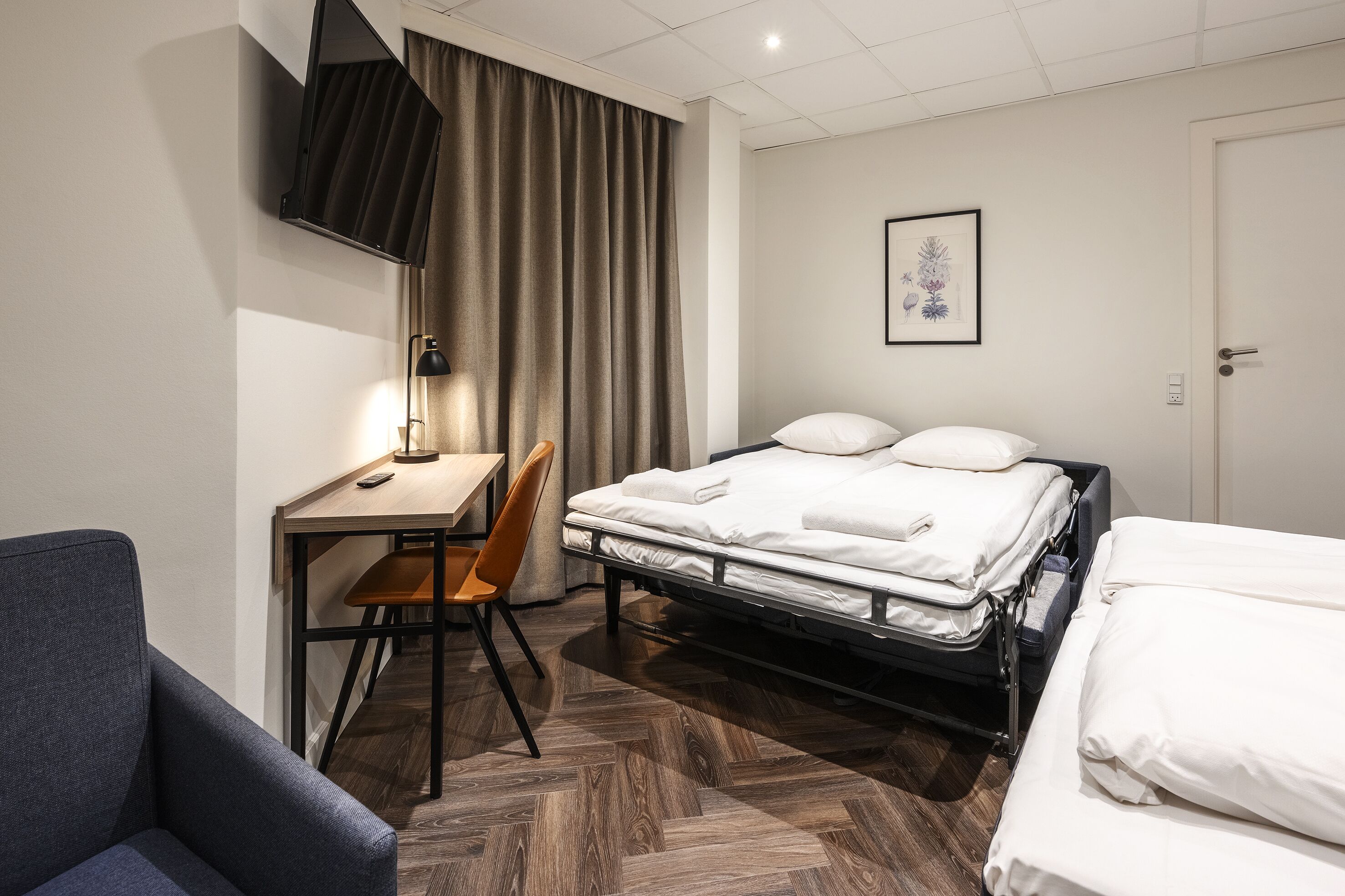 A hotel room with a bed, a desk, a chair, and a TV.