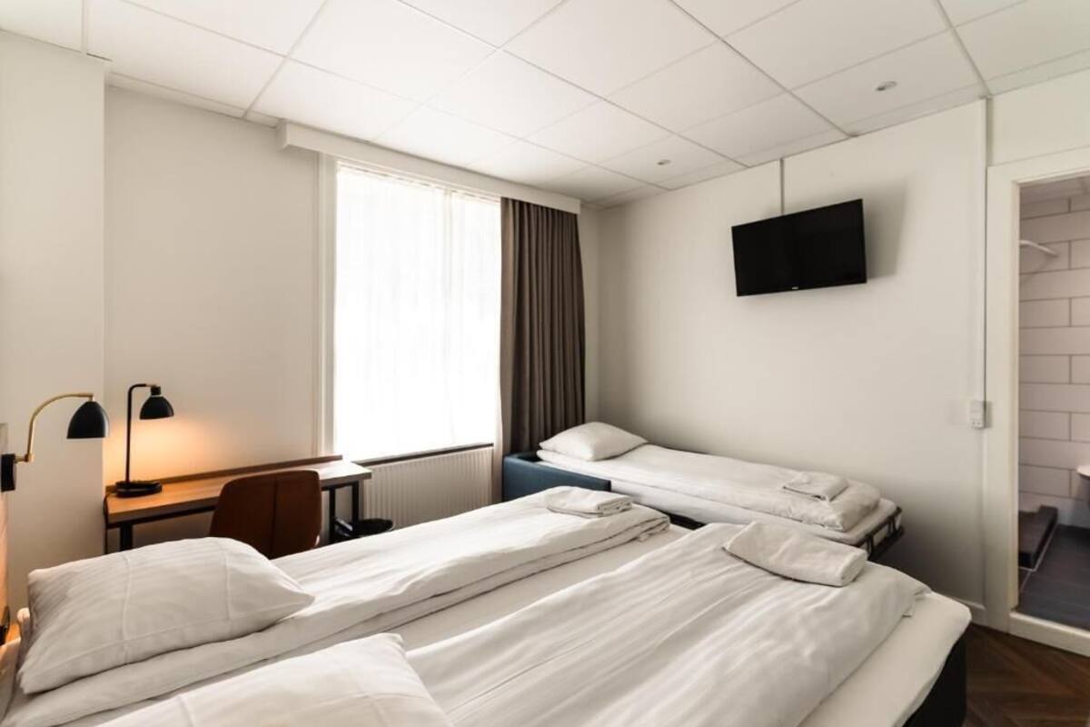 Une chambre d’hôtel avec deux lits, un bureau, une chaise, une télévision et une fenêtre avec des rideaux.