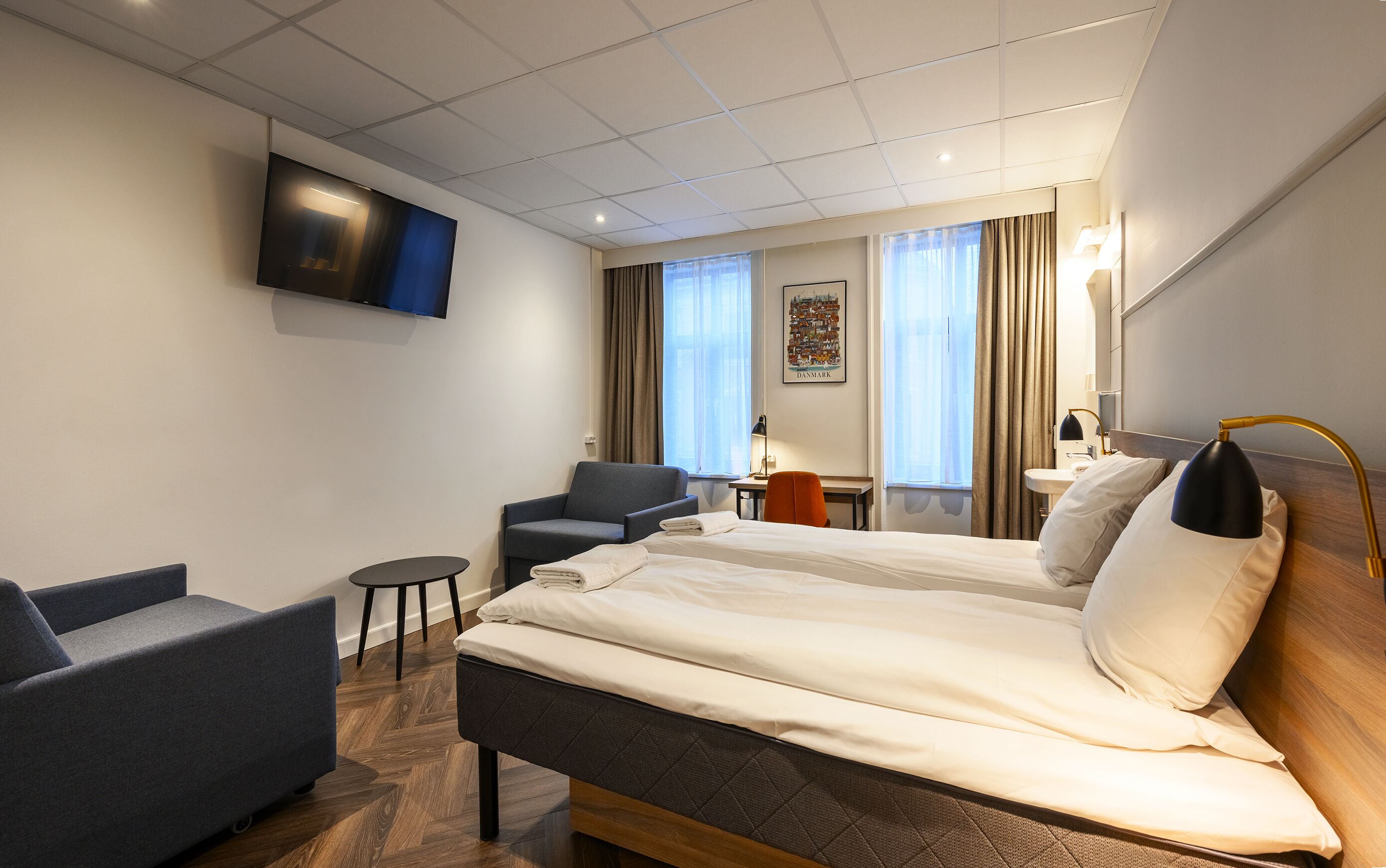 Una camera d'albergo con due letti, una scrivania, una sedia, una televisione e una finestra con tende.