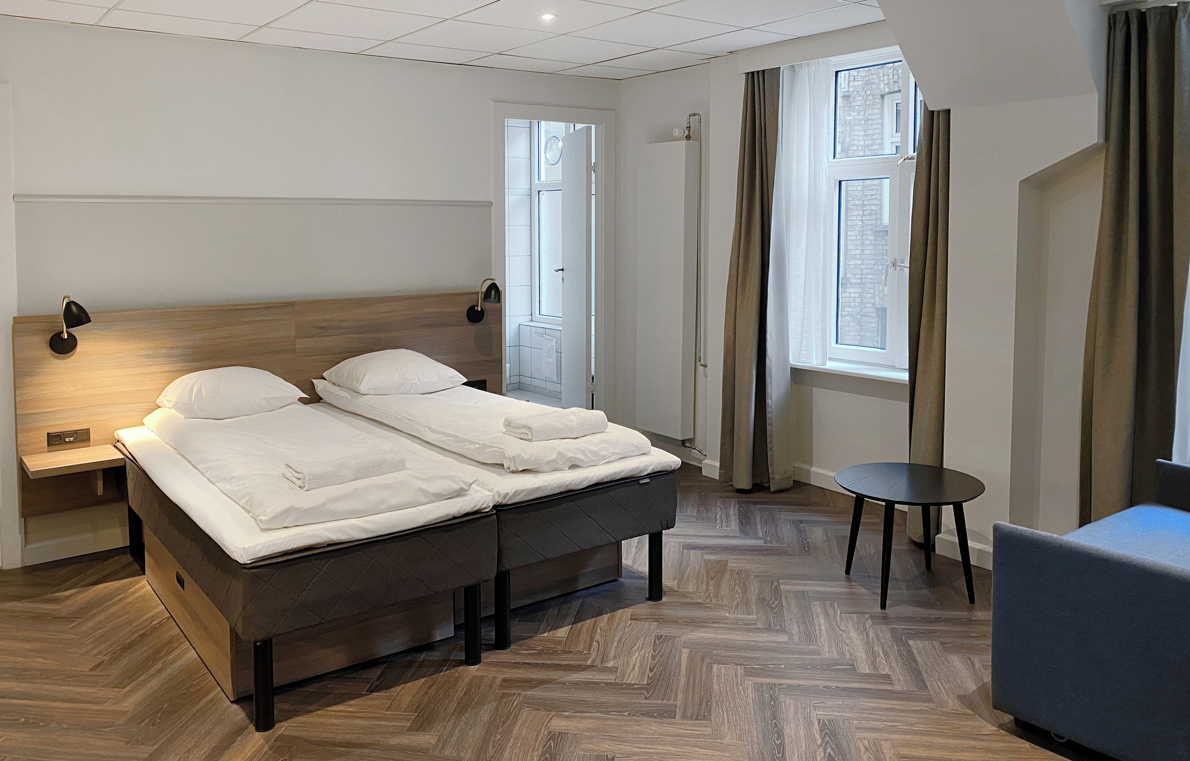 Ein modernes Hotelzimmer mit einem Doppelbett, Nachttischen, einem kleinen runden Tisch und einer Couch.