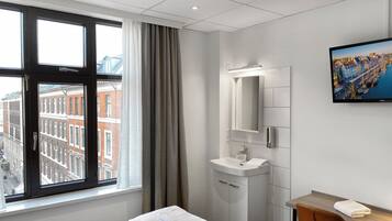 Ein Hotelzimmer mit Bett, Schreibtisch, Badezimmer mit Waschbecken und einem großen Fenster mit Blick auf die Stadt.