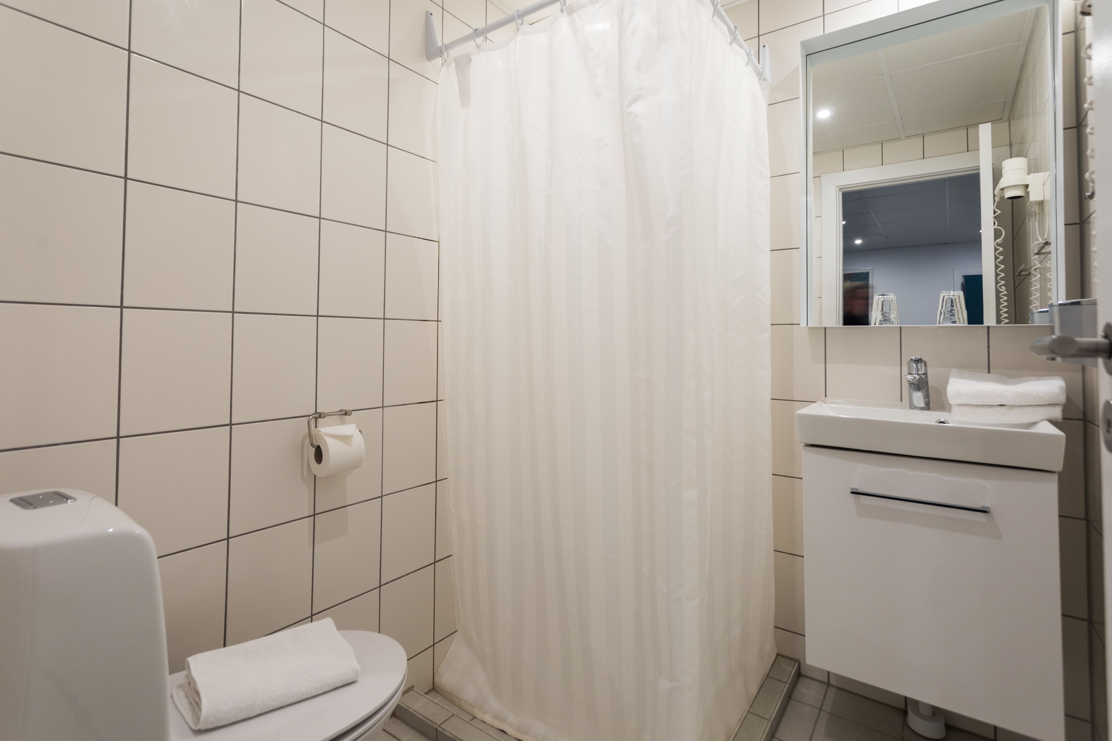 A bathroom with a toilet, a shower curtain, a sink, and a mirror.