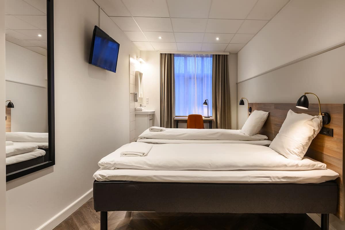 Une chambre d’hôtel avec un grand lit, un bureau avec une chaise, un téléviseur fixé au mur et une fenêtre avec des rideaux.