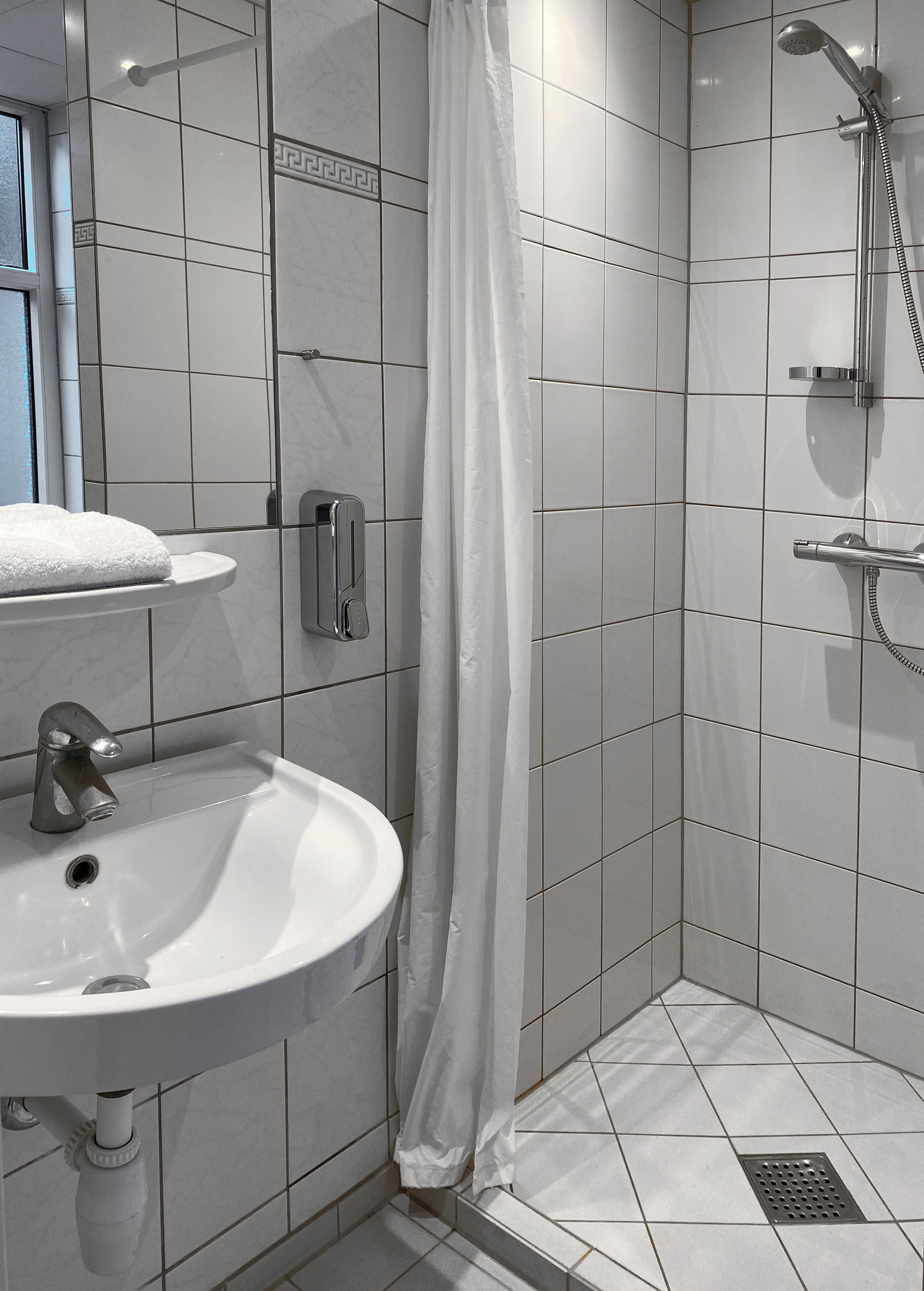 Un baño con lavamanos blanco, ducha con cabezal de ducha manual y cortina de ducha blanca.